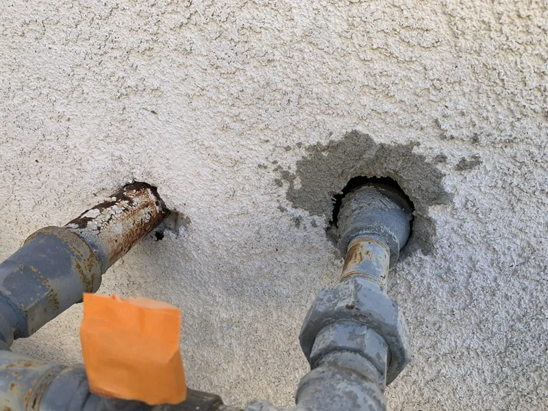 Stucco repair before, exposed rusted pipes and raw patch